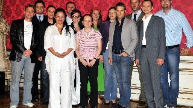 Eine Gruppe von Männern und Frauen posiert vor einer roten Wand mit floralem Muster.