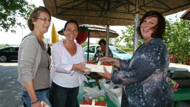 Drei Frauen stehen an einem Marktstand und verkaufen Erdbeeren.