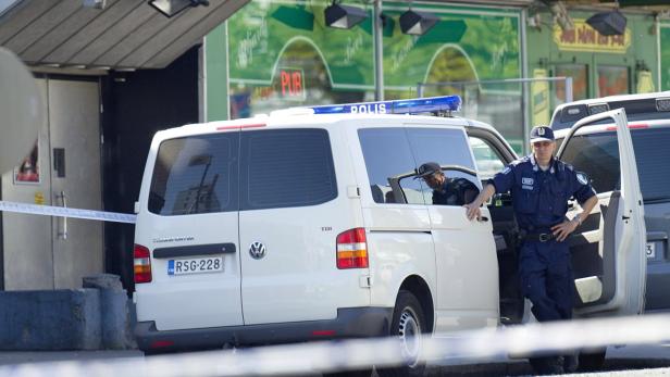 Ein Polizist steht an einem weißen Polizeiwagen vor einem Pub.