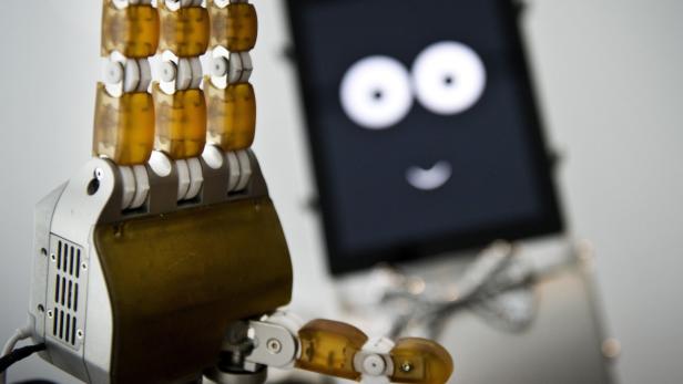 Eine Roboterhand vor einem Bildschirm mit einem einfachen Smiley-Gesicht.