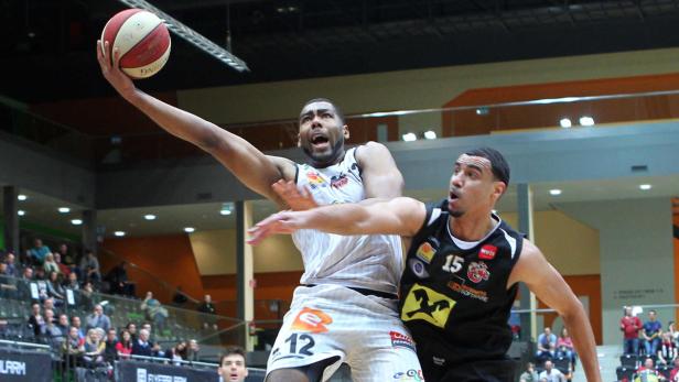 Zwei Basketballspieler während eines Spiels, einer im Sprung mit dem Ball in der Hand.