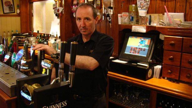 Ein Barkeeper steht hinter der Theke in einem Pub mit Zapfhähnen für Guinness und Bulmers.