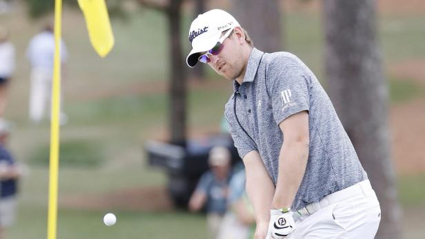 Ein Golfspieler schlägt einen Ball in Richtung eines gelben Lochstocks.
