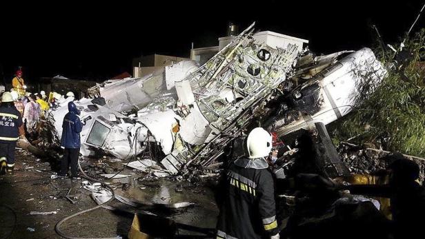 Einsatzkräfte stehen vor den Trümmern eines abgestürzten Flugzeugs.