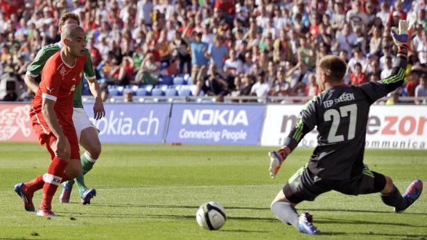 Ein Fußballspieler in Rot schießt auf das Tor, während der Torwart mit der Nummer 27 abwehrt.