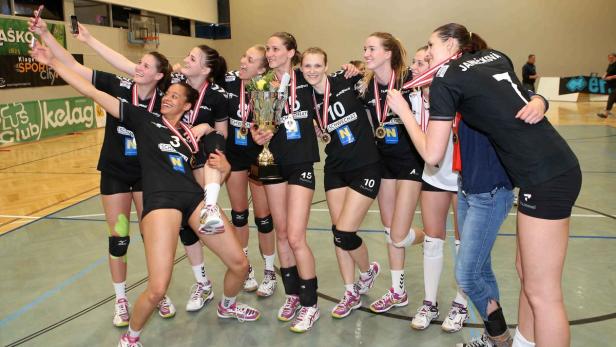Eine Volleyballmannschaft feiert mit einem Pokal und macht ein Selfie.
