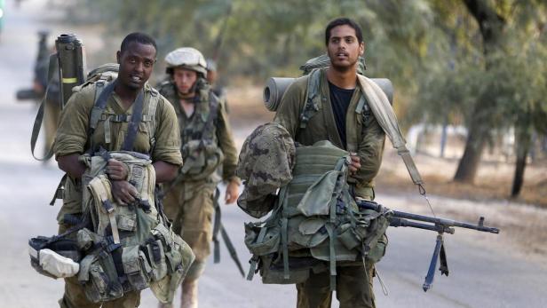 Drei Soldaten in Uniform tragen Ausrüstung auf einer Straße.