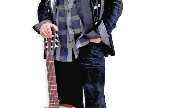 Ein Mann mit Hut und langer, blonder Perücke posiert mit einer Gitarre.