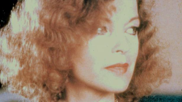 Nahaufnahme einer Frau mit lockigem Haar und rotem Lippenstift, die zur Seite blickt.