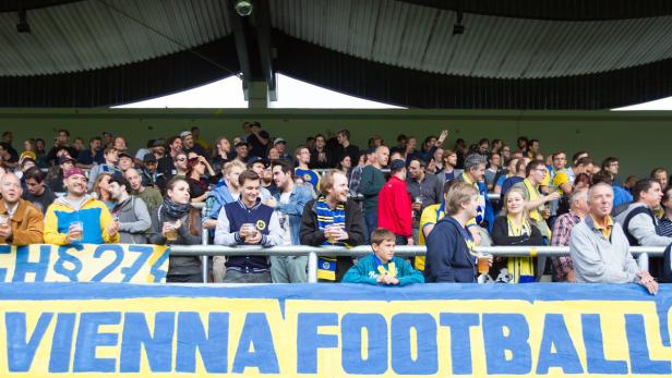 Zuschauer, viele mit Bier, auf einer Tribüne mit „Vienna Football“ Banner.