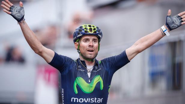 Ein Radrennfahrer im Movistar-Trikot jubelt mit erhobenen Armen.