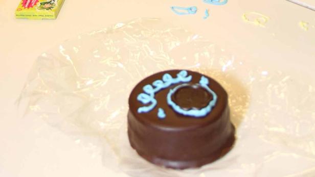 Ein Schokoladenkuchen mit blauer Zuckergussbeschriftung liegt auf einer Plastikfolie.