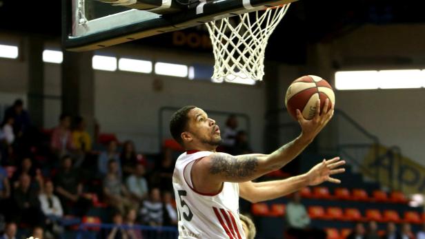 Ein Basketballspieler mit Tattoos wirft den Ball in Richtung Korb.