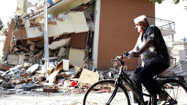 Ein älterer Mann fährt mit dem Fahrrad an einem durch ein Erdbeben zerstörten Gebäude vorbei.