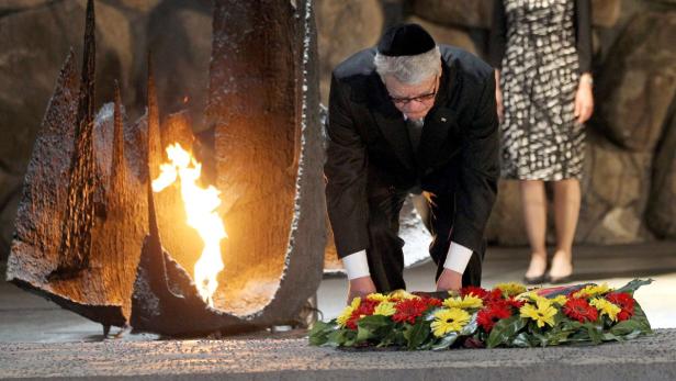 Ein Mann mit Kippa legt einen Kranz vor einer ewigen Flamme nieder.