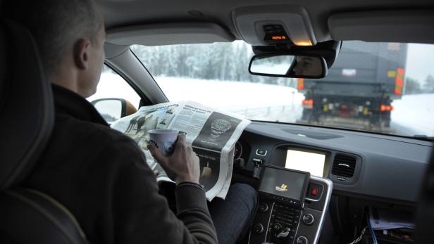 Ein Mann liest Zeitung und hält eine Tasse in einem fahrenden Auto.