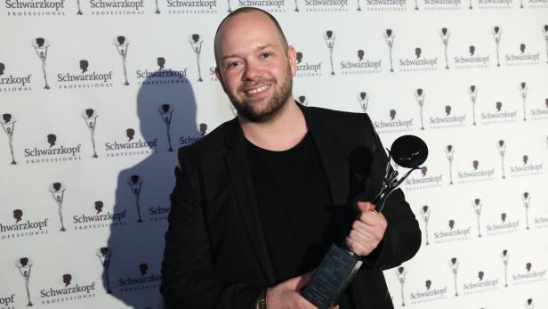 Ein Mann im schwarzen Sakko hält eine Auszeichnung von Schwarzkopf Professional.