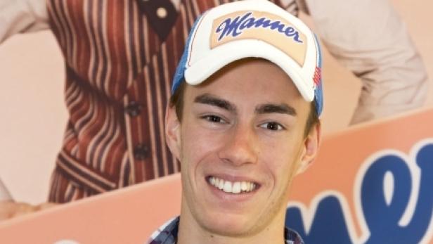 Ein junger Mann mit einer „Manner“-Kappe lächelt in die Kamera.