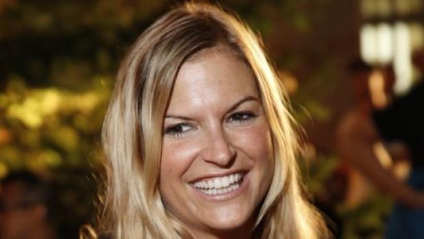 Eine lächelnde Frau mit blonden Haaren vor einem unscharfen Hintergrund.