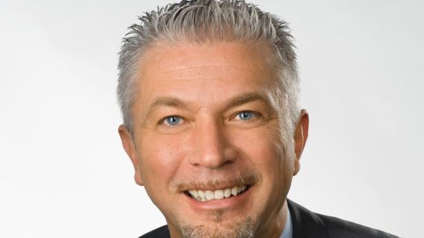 Porträt eines lächelnden Mannes mit grauen Haaren und blauen Augen.