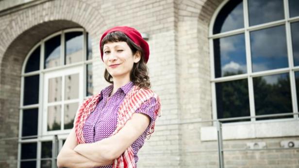 Eine Frau mit roter Baskenmütze zwinkert vor einem Gebäude.