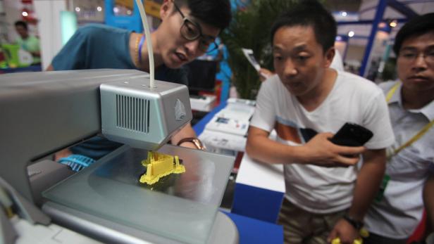 Zwei Männer beobachten einen 3D-Drucker, der ein gelbes Objekt herstellt.