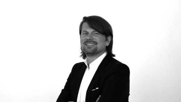 Ein Mann mit dunklem Haar und Anzug lächelt in die Kamera.