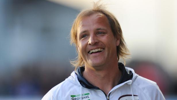 Ein lächelnder Mann mit blonden Haaren und einer weißen Jacke.