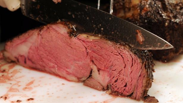 Ein Messer schneidet ein Stück Roastbeef an, das auf einem Schneidebrett liegt.