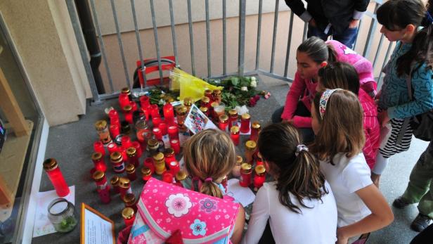 Eine Gruppe von Kindern steht vor einer Gedenkstätte mit Kerzen und Blumen.