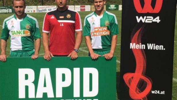 Drei Männer posieren mit einem Schild von Rapid Wien und einem W24-Banner.