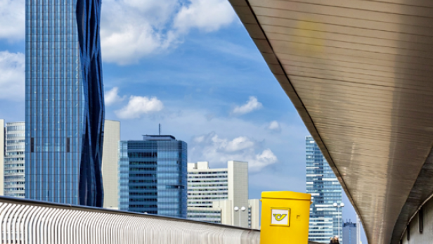 Eine Person in einem gelben Postkasten-Kostüm geht auf einer Brücke in Wien.