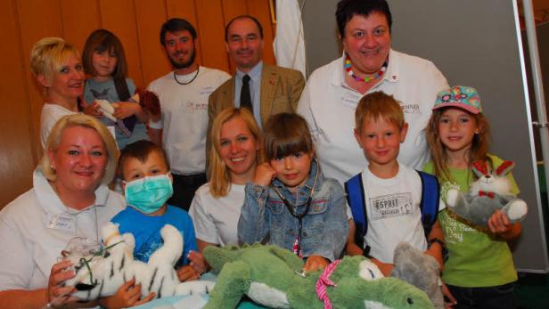 Kinder und Erwachsene spielen im Krankenhaus mit Stofftieren Arzt und Patient.