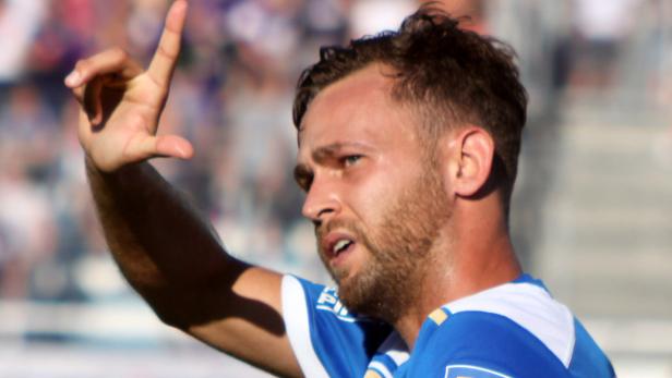 Ein Fußballspieler in einem blauen Trikot gestikuliert mit der Hand.