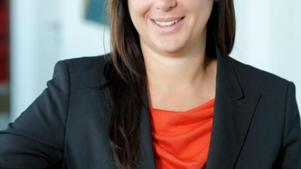 Eine lächelnde Frau in einem schwarzen Blazer und einem roten Oberteil posiert für ein Porträt.