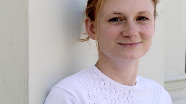 Eine Frau mit blonden Haaren lehnt an einer Wand.