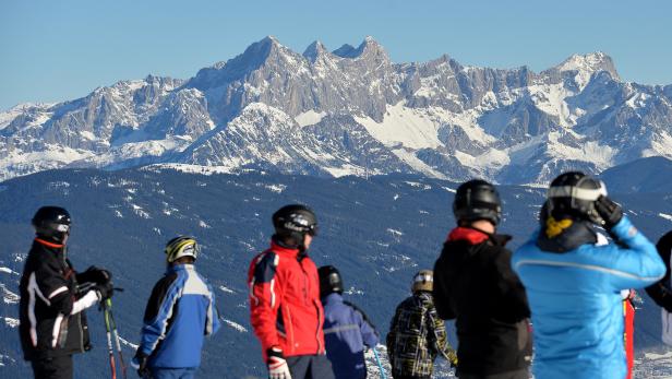 Symbolbild. Skifahrer stehen in Flachau auf einer Piste vor dem Dachsteinmassiv