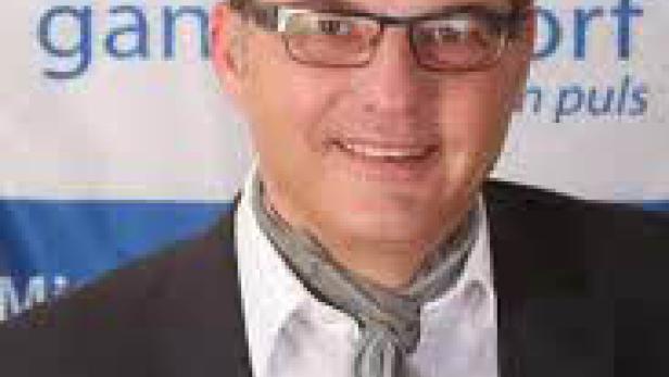 Ein Mann mit Brille und Schal lächelt in die Kamera.