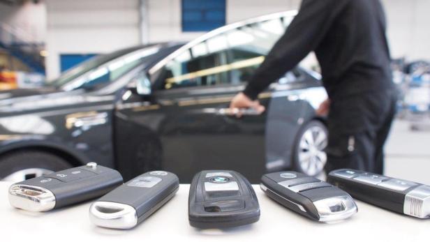 Mehrere Autoschlüssel liegen vor einem dunklen Auto.
