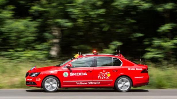 Ein roter Škoda, das offizielle Fahrzeug der Tour de France, fährt auf einer Straße.