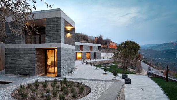 Ein modernes Gebäude mit grauer Fassade und großen Fenstern in einer hügeligen Landschaft.