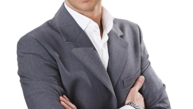 Ein Mann mit Brille und Anzug hat die Arme verschränkt.