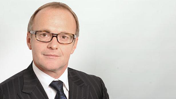 Ein Mann mit Brille und Anzug vor einem hellen Hintergrund.