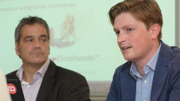 Zwei Männer sitzen vor einer Präsentation über Einzelhandel.