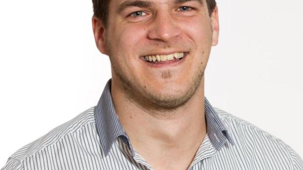 Ein lächelnder Mann mit kurzem, dunklem Haar und einem gestreiften Hemd vor einem weißen Hintergrund.