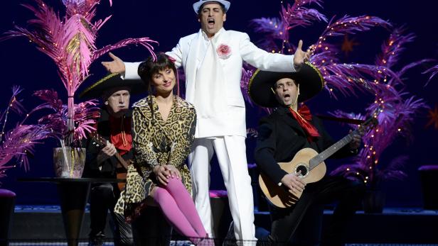 Eine Gruppe von Musikern tritt auf einer Bühne mit rosa Palmen im Hintergrund auf.