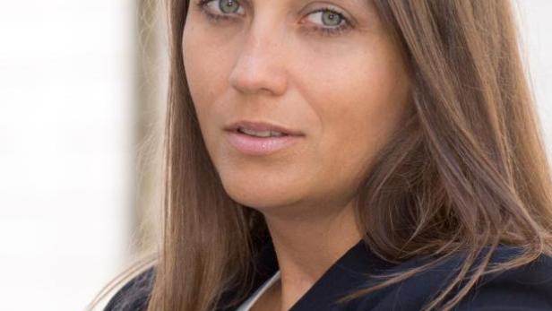 Eine Frau mit langen braunen Haaren und einem schwarzen Blazer blickt in die Kamera.