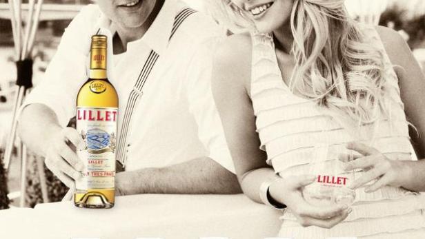 Ein Mann und eine Frau präsentieren eine Flasche und verschiedene Gläser Lillet-Aperitif.