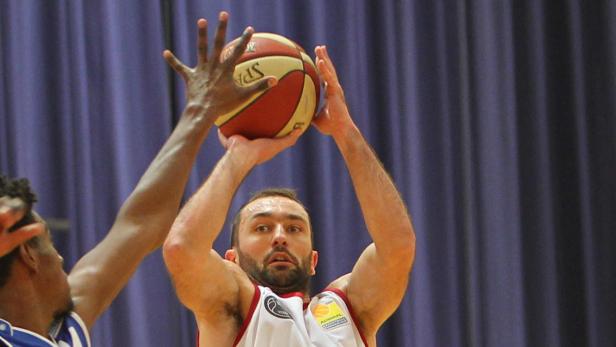 Ein Basketballspieler bereitet sich auf einen Wurf vor, während ein Gegenspieler ihn zu blocken versucht.