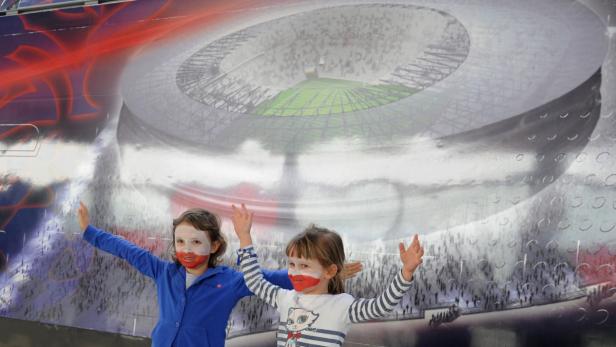 Zwei Mädchen mit polnischen Flaggen auf ihren Gesichtern posieren vor einem Bild von einem Stadion.